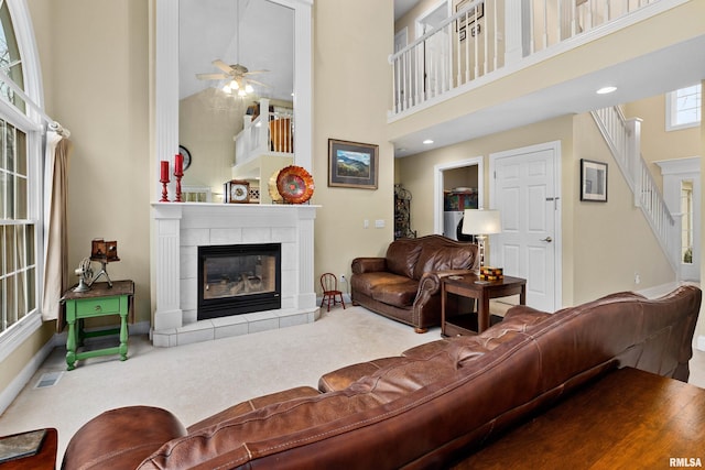 living room featuring ceiling fan, carpet floors, a high ceiling, and a tiled fireplace