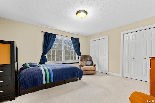 bedroom with light colored carpet, a textured ceiling, and multiple closets