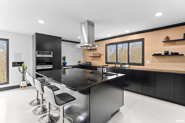 kitchen featuring open shelves, island range hood, modern cabinets, dark cabinets, and a kitchen bar