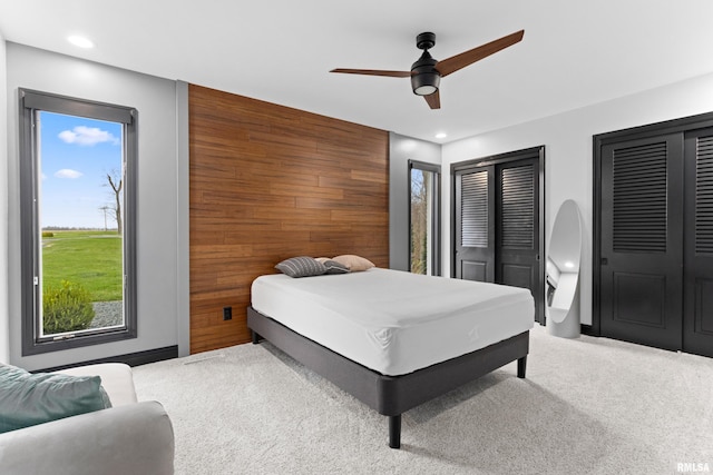 bedroom featuring recessed lighting, light colored carpet, an accent wall, a ceiling fan, and wood walls