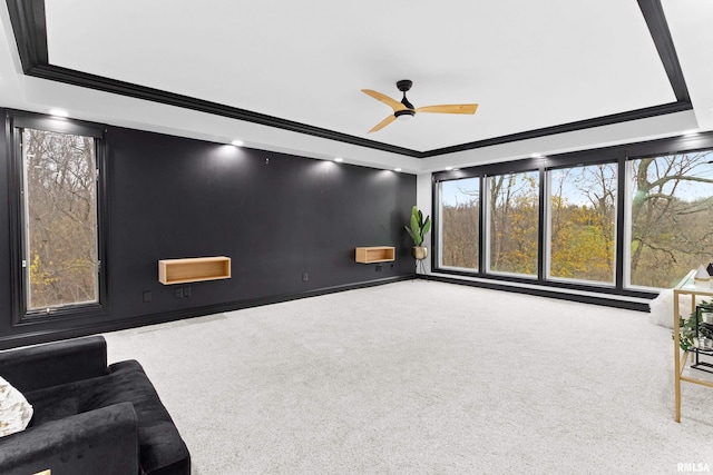 carpeted living room featuring baseboards, ornamental molding, a raised ceiling, and a ceiling fan