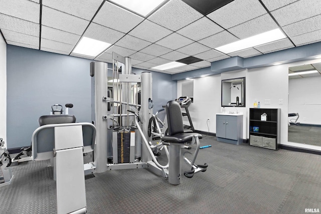 exercise room with a paneled ceiling, a sink, and baseboards