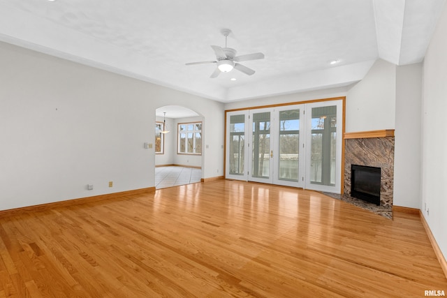 unfurnished living room with a high end fireplace, light wood-type flooring, and ceiling fan