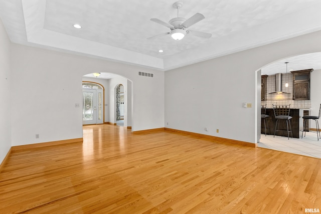 unfurnished living room featuring light wood-type flooring, a tray ceiling, and ceiling fan