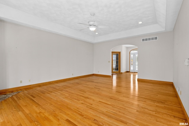 unfurnished room with a raised ceiling, french doors, light hardwood / wood-style flooring, and ceiling fan