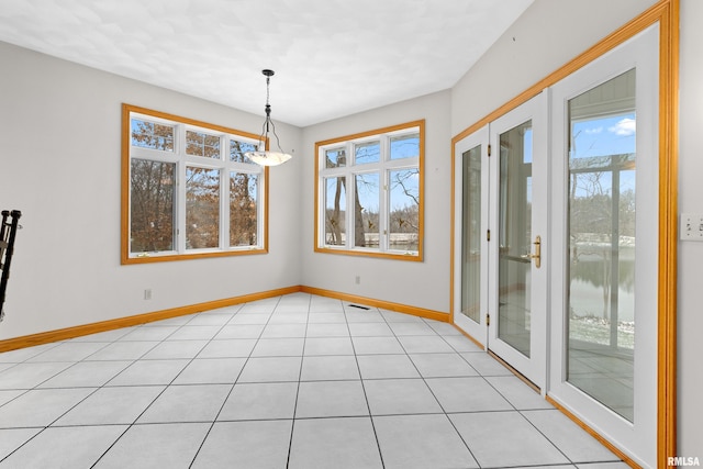 unfurnished dining area with a water view, plenty of natural light, light tile patterned floors, and french doors