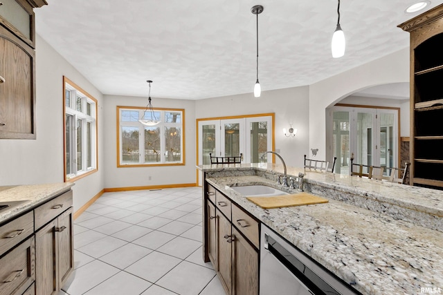 kitchen with light stone countertops, french doors, hanging light fixtures, and sink