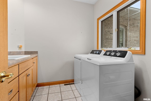 clothes washing area with cabinets, washing machine and dryer, light tile patterned floors, and sink