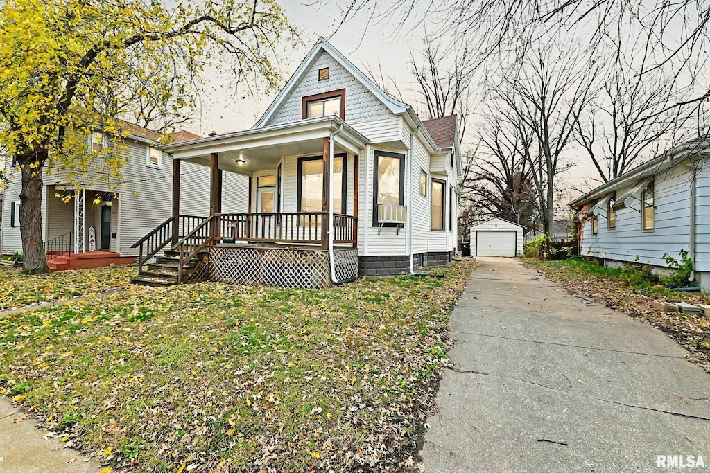 victorian home with a front yard, a detached garage, a porch, and an outbuilding