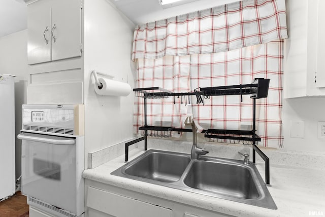 kitchen with white oven, white cabinetry, and sink