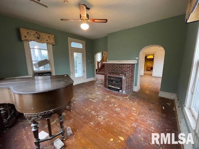 unfurnished living room with ceiling fan, wood-type flooring, and a brick fireplace