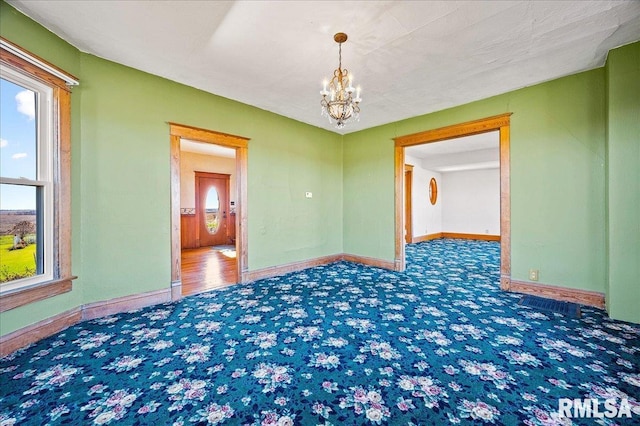 unfurnished room with an inviting chandelier, plenty of natural light, and dark colored carpet