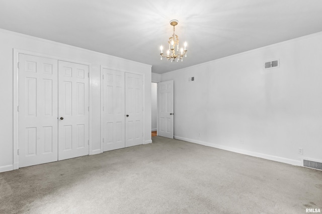 unfurnished bedroom featuring carpet, a notable chandelier, ornamental molding, and two closets