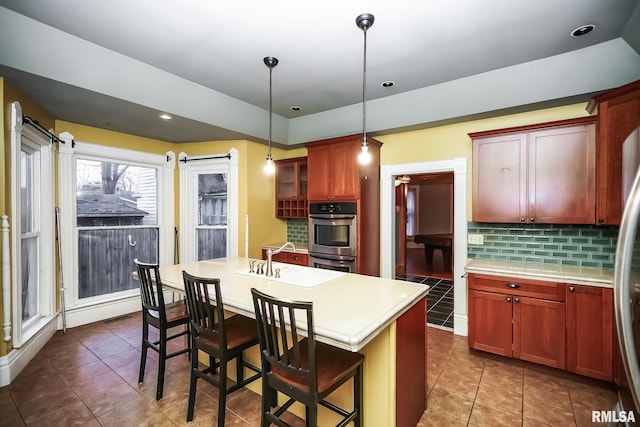 kitchen featuring tasteful backsplash, double oven, pendant lighting, a kitchen bar, and a kitchen island with sink