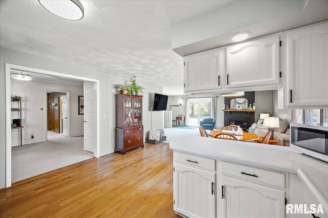 kitchen with a fireplace, white cabinetry, and light hardwood / wood-style flooring