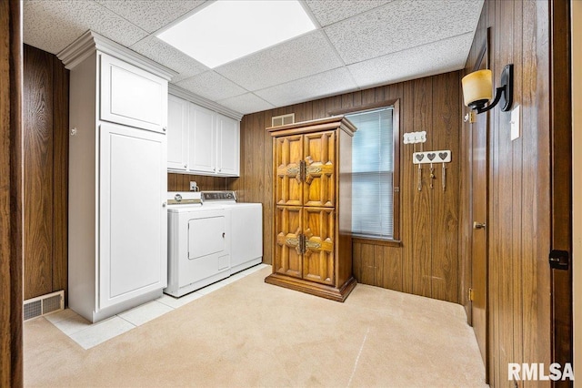 laundry room featuring washing machine and dryer, light carpet, wooden walls, and cabinets