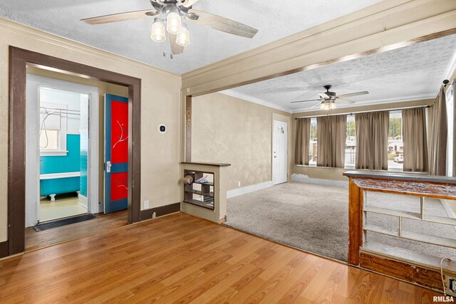 unfurnished living room with ceiling fan, hardwood / wood-style floors, a textured ceiling, and ornamental molding