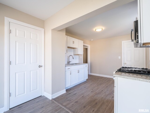 kitchen featuring white cabinets, hardwood / wood-style floors, light stone countertops, and sink