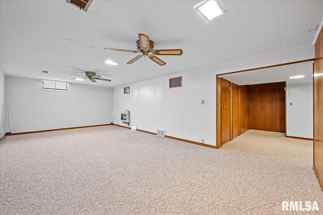 empty room with heating unit, wooden walls, carpet floors, and ceiling fan