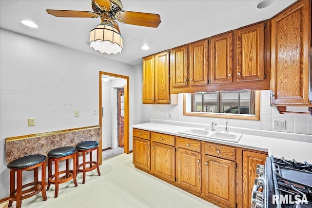 kitchen featuring sink, gas range, ceiling fan, decorative backsplash, and a breakfast bar area