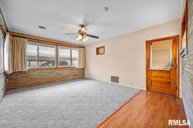 unfurnished room featuring hardwood / wood-style flooring, ceiling fan, and brick wall