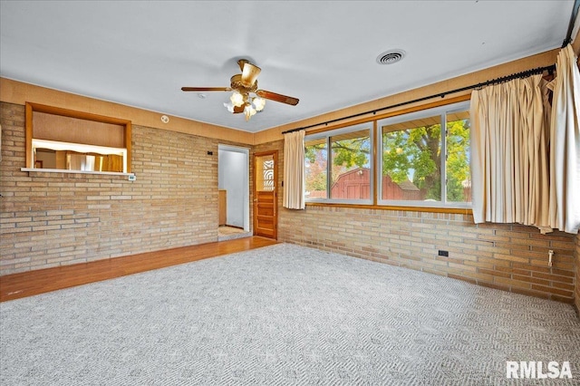 unfurnished living room featuring carpet, ceiling fan, and brick wall