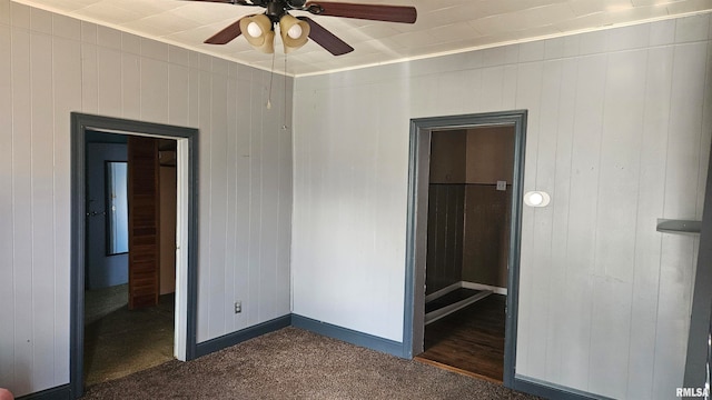 unfurnished bedroom featuring dark carpet, ceiling fan, and wooden walls