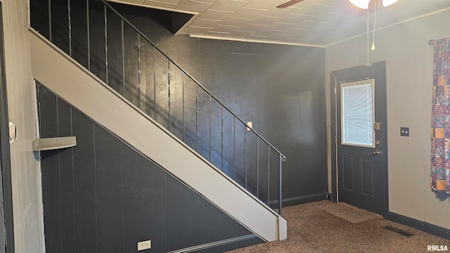 entrance foyer featuring ceiling fan, carpet floors, ornamental molding, and wooden walls