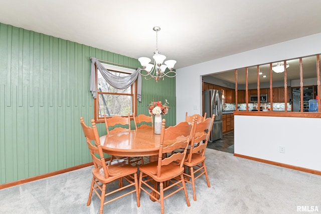 carpeted dining space featuring wood walls and a chandelier