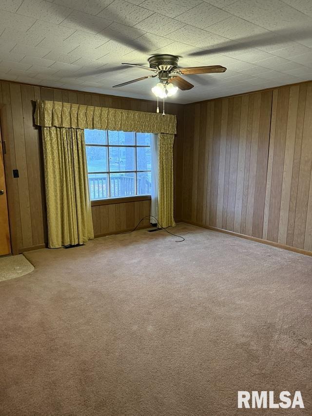 empty room with carpet, ceiling fan, and wood walls