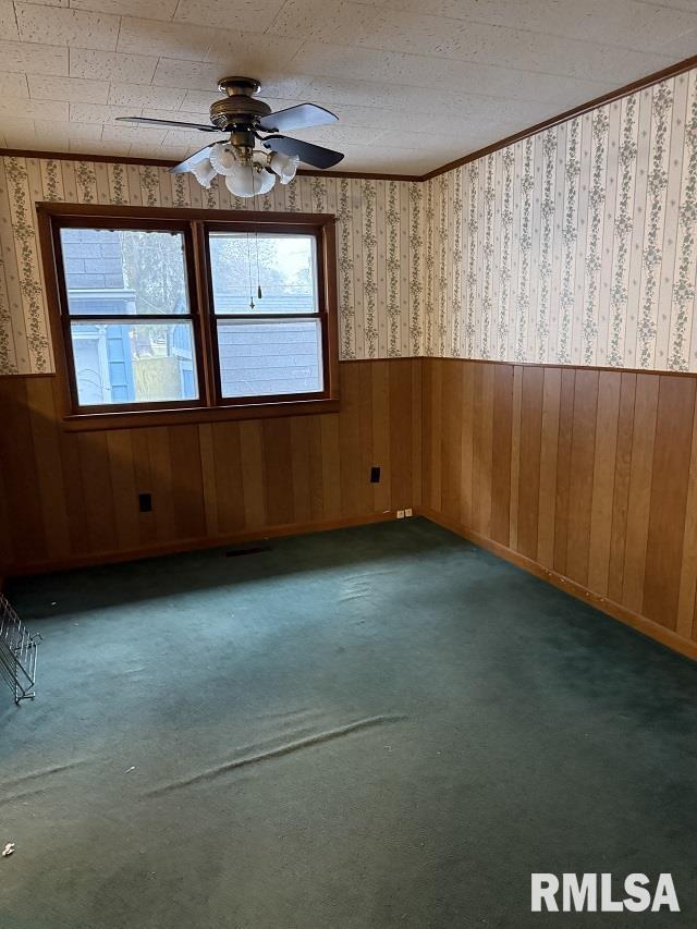 carpeted spare room featuring wooden walls and ceiling fan