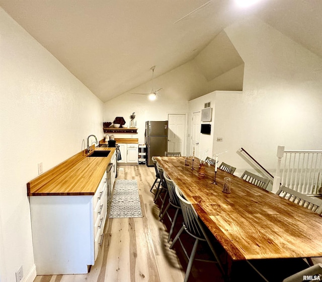 kitchen featuring sink, light hardwood / wood-style flooring, stainless steel refrigerator, white cabinets, and vaulted ceiling