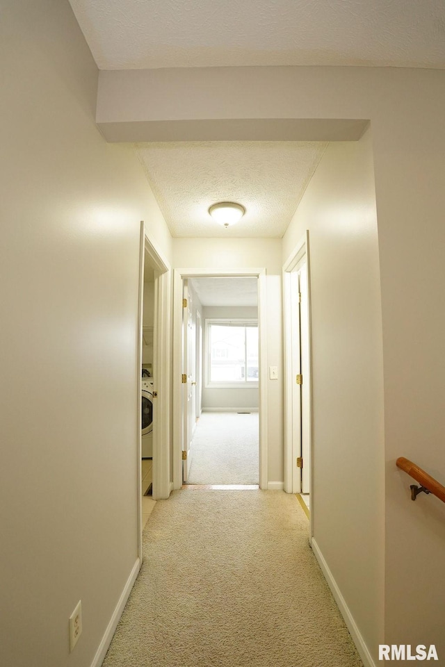 hall with light colored carpet, a textured ceiling, and washer / clothes dryer