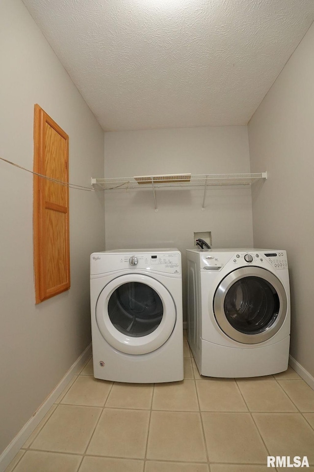 laundry area with washer and dryer, a textured ceiling, and light tile patterned flooring