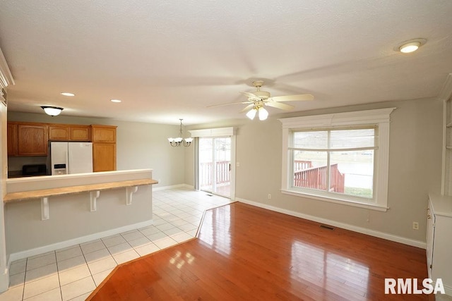 kitchen featuring pendant lighting, ceiling fan with notable chandelier, light wood-type flooring, white fridge with ice dispenser, and a breakfast bar area