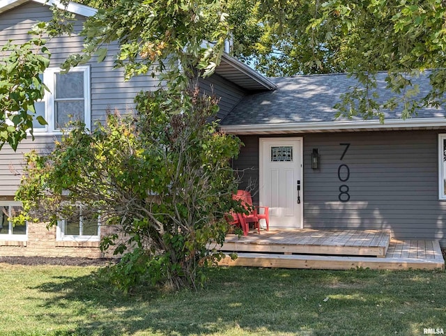 entrance to property with a shingled roof, a lawn, and a wooden deck