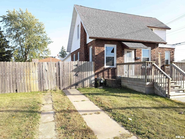 view of front facade featuring a front lawn, a shingled roof, fence, and brick siding