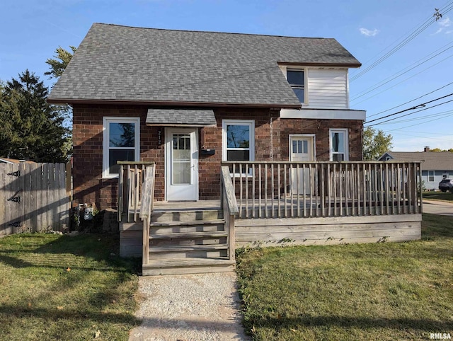 view of front of house featuring a front lawn, a shingled roof, fence, and brick siding