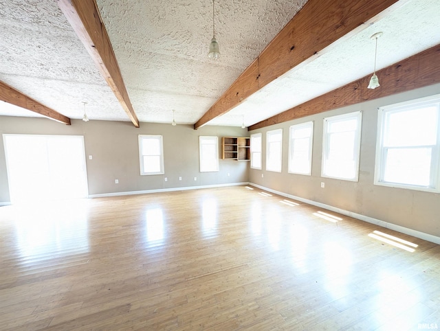 empty room featuring beam ceiling, a textured ceiling, and light wood-type flooring