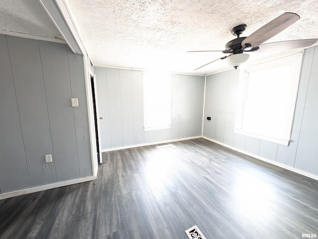 empty room featuring a textured ceiling, dark wood-type flooring, a ceiling fan, and baseboards