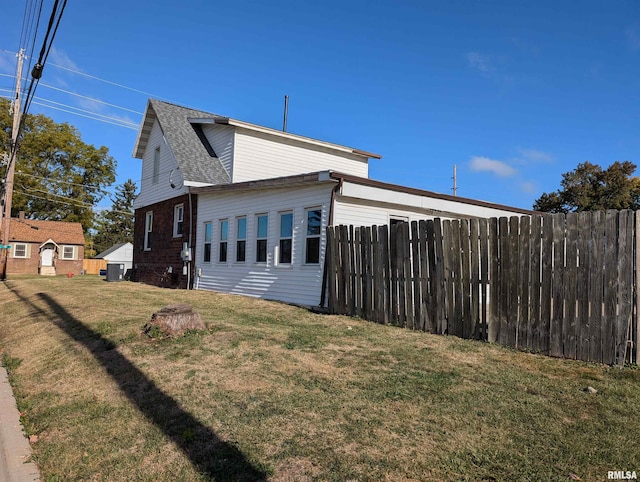 view of side of property with roof with shingles, fence, and a yard