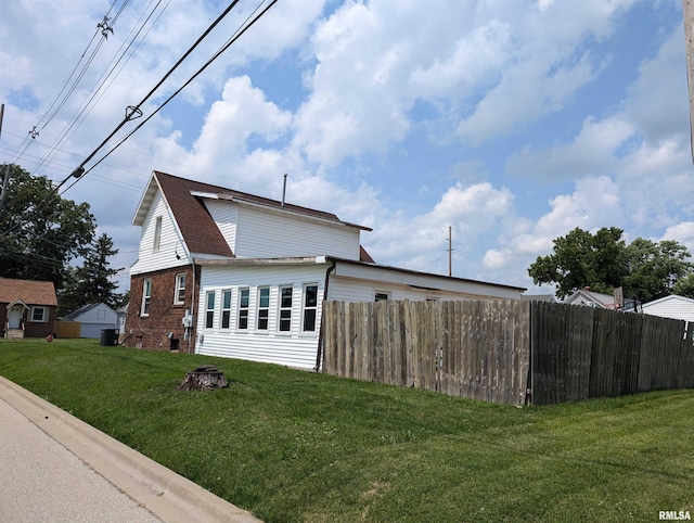 view of side of home with brick siding, a lawn, a shingled roof, and fence