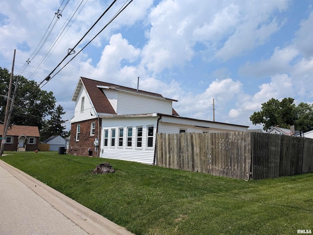 view of side of property with a yard, brick siding, fence, and roof with shingles