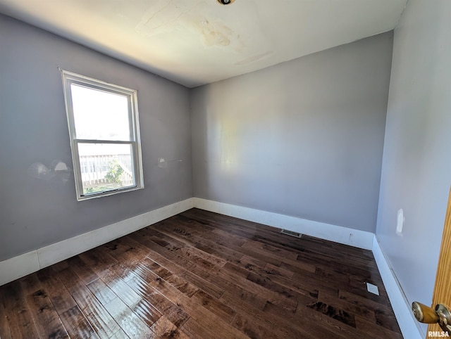 spare room featuring dark wood-type flooring, visible vents, and baseboards