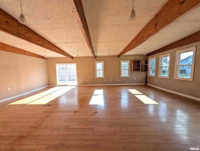 empty room featuring beamed ceiling, wood finished floors, and baseboards