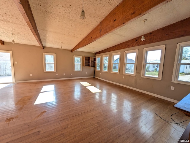 empty room featuring vaulted ceiling with beams, a textured ceiling, wood-type flooring, and baseboards