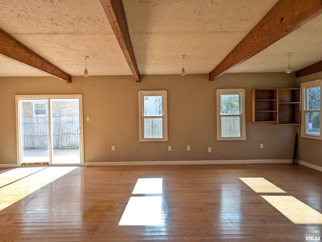 unfurnished room with a textured ceiling, wood finished floors, beam ceiling, and baseboards