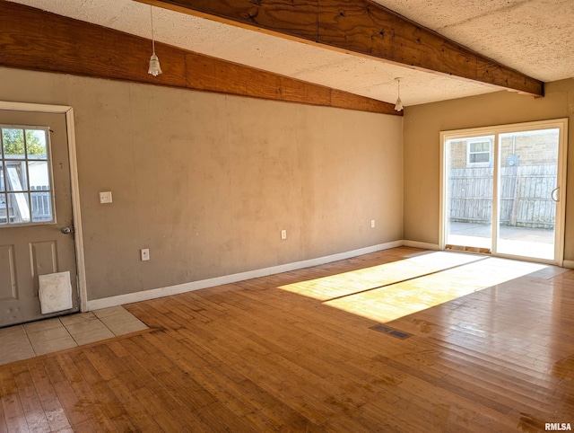 interior space featuring a textured ceiling, beam ceiling, hardwood / wood-style flooring, and baseboards