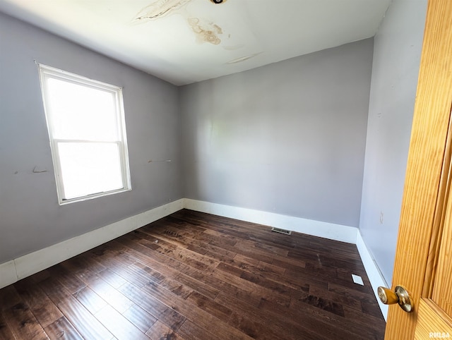 empty room with dark wood finished floors, visible vents, and baseboards