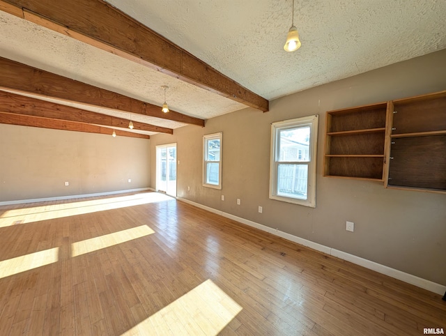 unfurnished room with a textured ceiling, beamed ceiling, wood-type flooring, and plenty of natural light